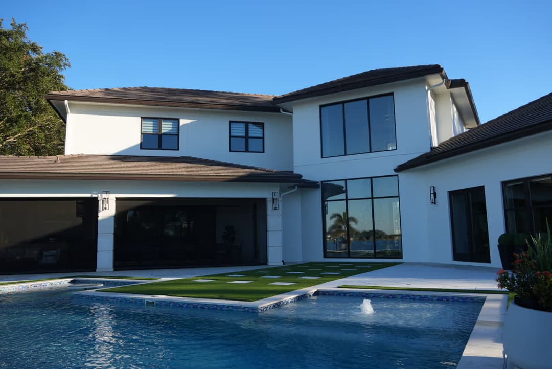 Modern luxury home with spacious patio, pool, and lush landscaping under clear blue sky.