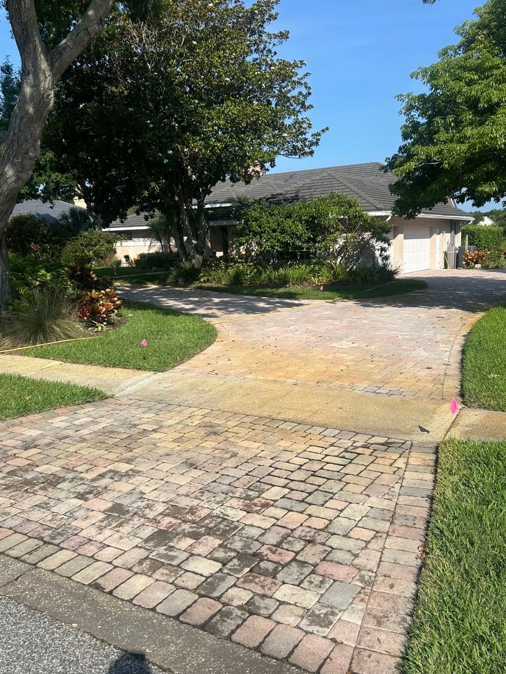 Paved driveway with patterned bricks, surrounded by greenery and a residential home.